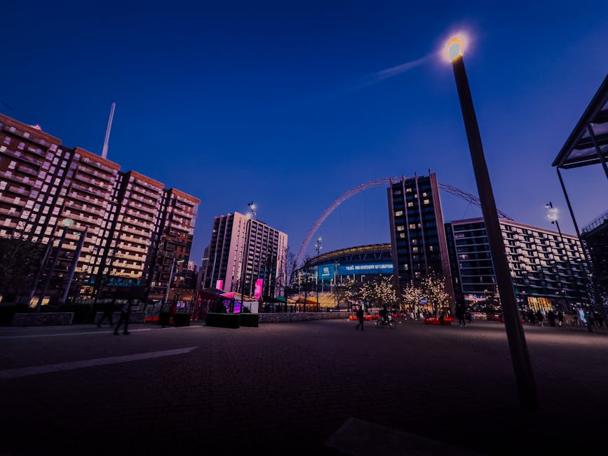 The image depicts the exterior entrance of Wembley Park Station with a large, prominent sign displaying the words 'Wembley Park' in bold, capitalized silver letters mounted on a metallic frame. The st